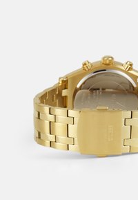 Guld rustfrit stål ur med en poleret finish, der har et kraftigt armbåndsdesign, tre krone-detaljer og et spænde med indgraveret "GUTSS."