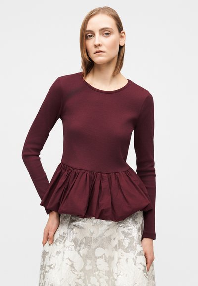 Bluza cu mâneci lungi, culoare burgundy, cu textură striată și tiv peplum adunat, asortată cu o fustă argintie cu model floral.