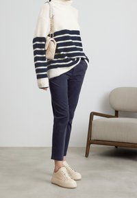 Vit och marinrandig polotröja, marinblå slim-fit byxor och beige sneakers. Innehåller en axelväska i ett lätt texturerat material.