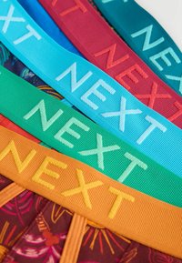 Ceintures en tissu de couleurs vives avec le mot «NEXT» brodé, disposées en rangées diagonales qui se chevauchent.