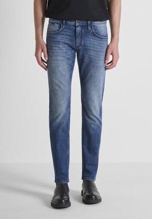 Jeans de mezclilla azul ajustados con un acabado desgastado, cinco bolsillos y cierre de botón. Combinados con botas negras hasta el tobillo para crear contraste.