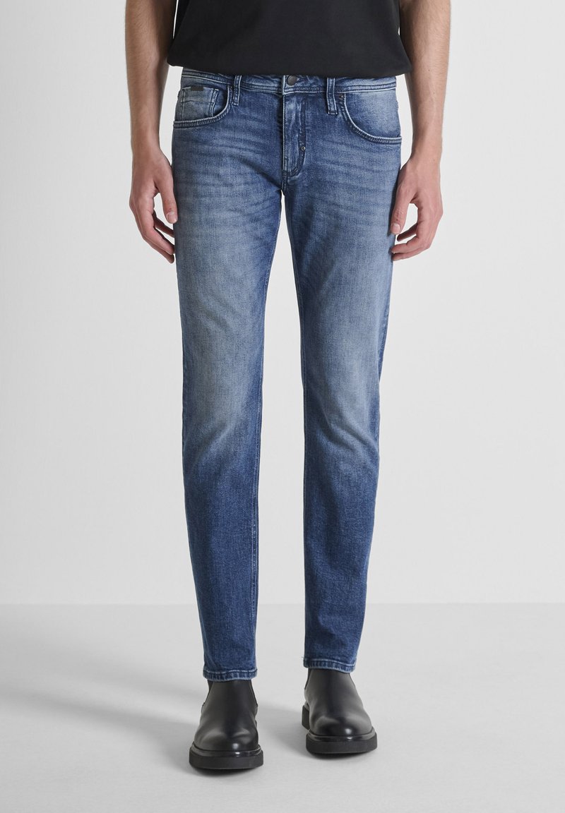 Jeans de mezclilla azul ajustados con un acabado desgastado, cinco bolsillos y cierre de botón. Combinados con botas negras hasta el tobillo para crear contraste.