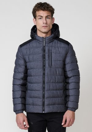 Chaqueta acolchada gris con capucha, presenta un diseño de tela texturizada, patrón acolchado, paneles en negro en los hombros y bolsillos frontales con cremallera.