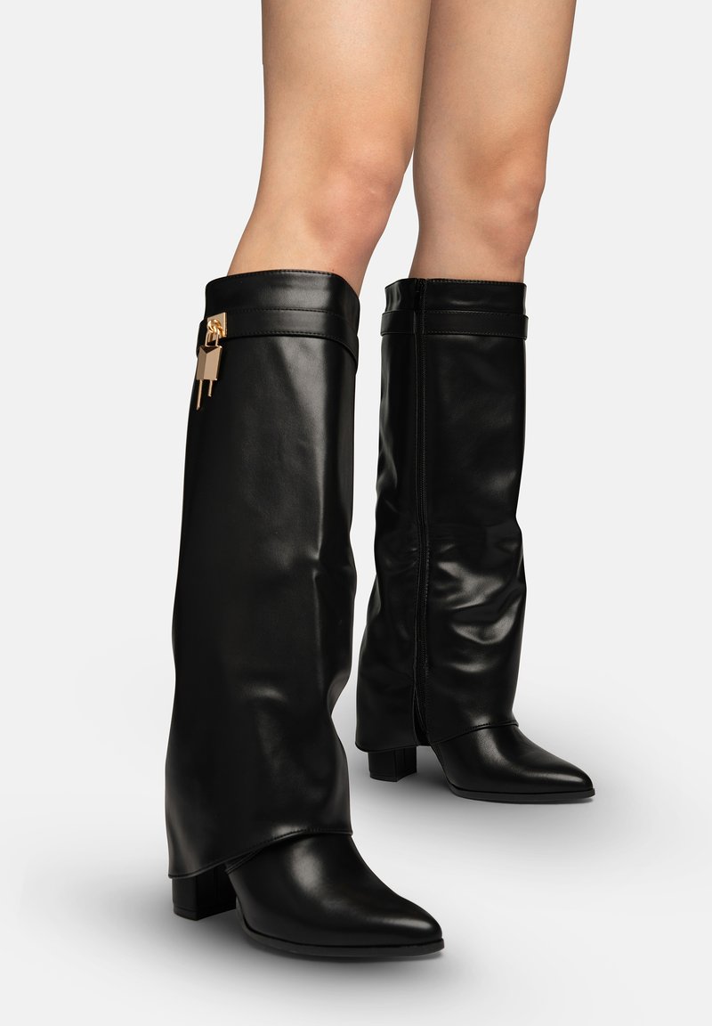 Botas negras de cuero hasta la rodilla con tacones bajos de bloque y un pequeño charm en forma de candado dorado en el lado exterior de la bota izquierda.