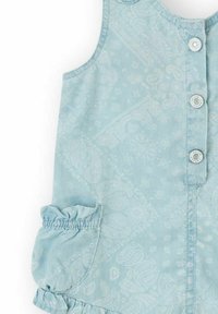 Peto de mezclilla azul claro con patrón de paisley, botones a presión, diseño sin mangas y bolsillos con volantes para un toque de textura y detalle adicional.
