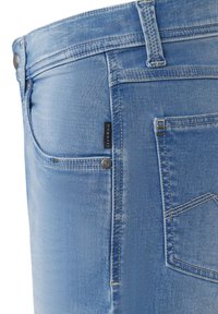 Hellblaue Jeans aus Denim mit glatter Textur, ausgestattet mit Reißverschluss, Knopfverschluss und einem kleinen Markenetikett neben der Tasche.