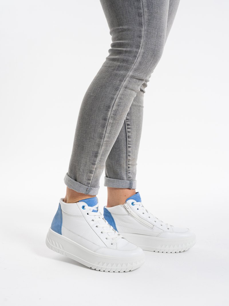 Person wearing white high-top sneakers with blue accents and gray rolled-up jeans, standing on white background.