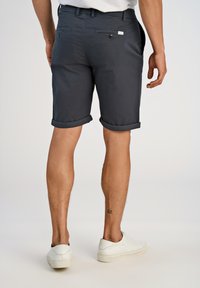 Navy blue shorts, joissa on slim fit -leikkaus ja käännetyt lahkeet. Takana on napilliset taskut ja pieni logo-etiketti vyötäröllä.