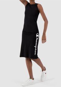 Czarna sukienka bez rękawów wykonana z miękkiego materiału o dopasowanym kroju. Posiada pionowo nadrukowane białe logo "Champion" na boku.