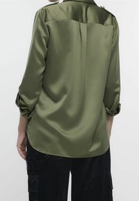 Olivgrön satinblus med trekvartslånga ärmar, med knäppta manschetter, en mjuk textur och en subtil sömdetalj längs ryggen.