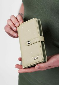 Světle zelená peněženka s bílými puntíky, na patent, se zlatým logem. Vyrobena z hladkého materiálu, má kompaktní design vhodný pro uchování karet.