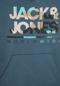Kék kapucnis pulóver, elülső zsebbel, merész, sokszínű "JACK & JONES WORLDWIDE" felirattal, különböző mintákkal és színkiegészítőkkel.
