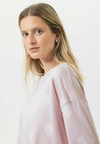 Haut rose clair à manches longues avec des pois blancs ; fabriqué en tissu doux ; présente une coupe décontractée et un design d'épaule tombante.
