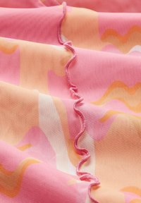 Tela texturizada de color rosa con patrones abstractos de ondas en naranja y blanco. Presenta un detalle de borde con volantes en un lado.