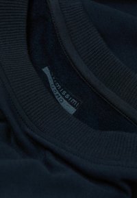 Marineblaues Kleidungsstück mit einem weichen, strukturierten Innenfutter. Verfügt über einen gerippten Ausschnitt und ein bedrucktes Etikett am Kragen. Glattes Gewebe sichtbar.