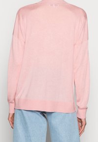 Personne portant un pull rose clair ample à manches longues et un pantalon en denim bleu clair, vue de dos.