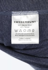 Ciemnoniebieska tkanina z etykietą "SWEDEMOUNT", zawierającą 60% wełny merino i 40% tencelu. Dołączone instrukcje dotyczące pielęgnacji. Gładka tekstura.