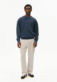 Marineblauwe trui met geribbelde manchetten, gecombineerd met lichtgrijze wijde broekspijpen en zwarte sneakers met witte veters. Eenvoudig, casual ontwerp.