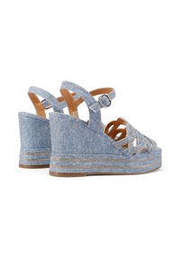 Sandali con zeppa in denim blu, design incrociato con cinturini, fibbia alla caviglia e piattaforma testurizzata. Accentuati da dettagli metallici lungo la suola.