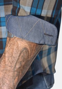 Langärmeliges, kariertes Hemd in Blau-, Braun- und Beigetönen. Die umgeschlagene Manschette zeigt diagonale Nähte und einen denimähnlichen Stoff.