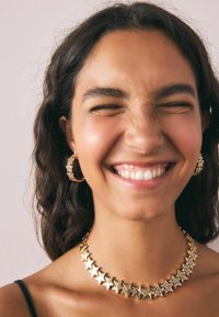 Colier în formă de stea aurie și cercei asortați cu accente texturate. Colierul are stele lucioase și stele cu puncte, alternate, într-un lanț continuu.