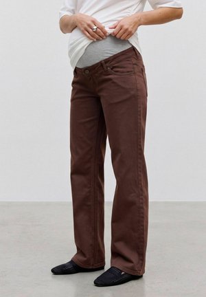 Personne portant un pantalon de maternité marron avec une ceinture élastique grise, montrée du milieu du torse aux pieds, ajustant une chemise blanche.
