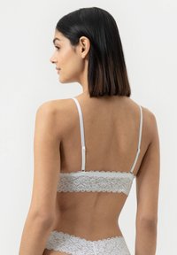 Witte kanten bralette met geschulpte randen en verstelbare bandjes. Heeft een sluiting aan de achterkant en een delicaat bloemmotief. Zachte textuur.