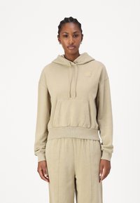 Beige hoodie med en frontficka, snörning i huvan och ribbad nederkant. Mjuk tyg med en liten logotyp på bröstet. Avslappnad passform.