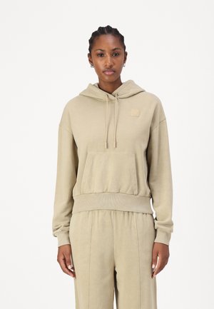 Beige hettegenser med frontlomme, snøring i hetten og ribbestrikket kant. Myk stoff med et lite logo-patch på brystet. Ledig passform.