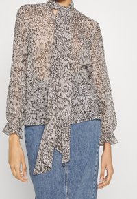 Gennemsigtig bluse i beige og grå dyreprint, med høj hals, lange ærmer med flæsemanchetter og et frontbånd.