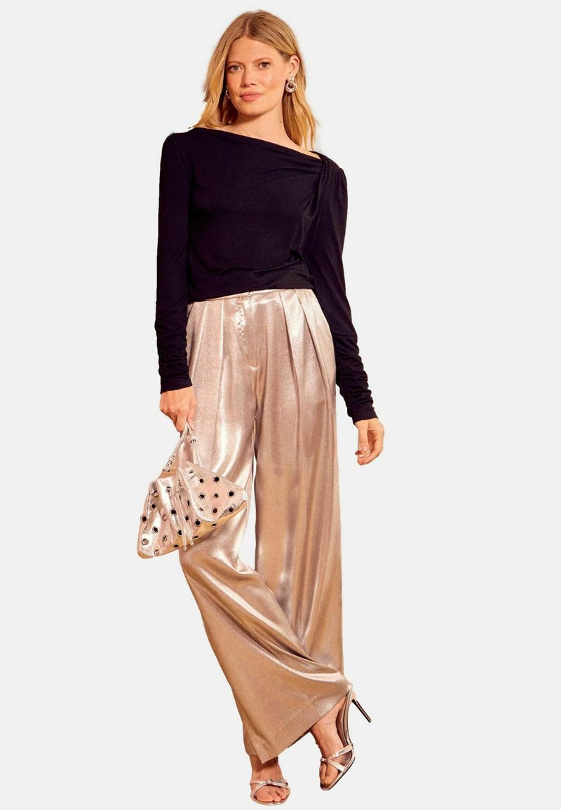 Fekete, hosszú ujjú felső, aszimmetrikus nyakkal, fényes, pliszírozott, fémes arany nadrággal párosítva. Ezüst magas sarkú szandál és mintás ezüst clutch.