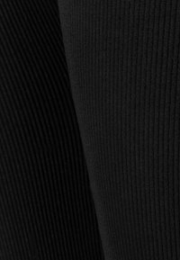 Zwart geribd stof die verschillende texturen laat zien; het ene gedeelte is glad, terwijl het andere verticale ribbels heeft voor extra detail.