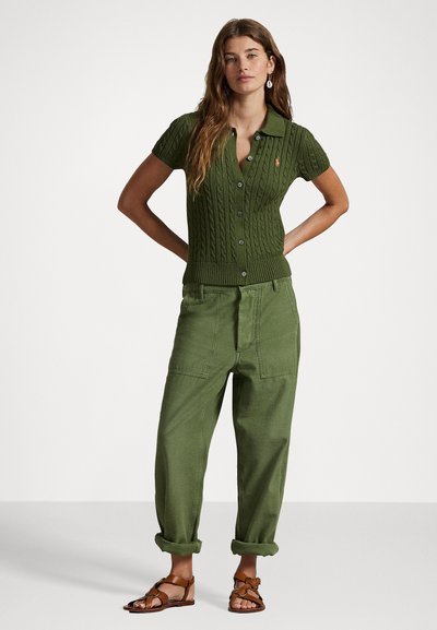 Groen kabelgebreid poloshirt met een kraag en korte mouwen, gecombineerd met hoge groene wijde broek en bruine sandalen met bandjes.