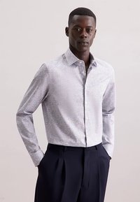 Camicia azzurro chiaro a maniche lunghe con motivo floreale, colletto con bottoni e tessuto strutturato, abbinata a pantaloni scuri.
