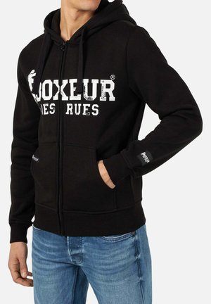 Black zip-up hoodie made of soft fabric, featuring a drawstring hood, front pockets, and white graphic text on the chest.