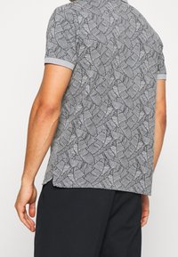 Polo gris à manches courtes avec un imprimé à motif de feuilles texturé et un col côtelé contrastant. Coupe légère et décontractée.