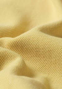 Tessuto giallo con un motivo texturizzato e intrecciato, che mostra morbide pieghe e curve. La superficie appare traspirante e leggera.