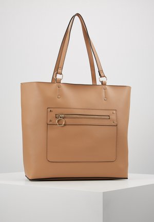 Tan lederen shopper met dubbele schouderbanden en een voorvak met ritssluiting en een ronde gouden ritssluiting, tentoongesteld op een wit voetstuk.