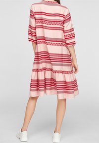 Roze jurk met rode en witte horizontale strepen, driekwart mouwen, een gelaagde rok en een geometrisch patroon langs de strepen.