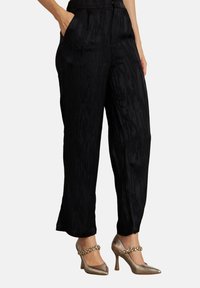 Zwarte wijde broek met zijzakken, gedragen met metalen hoge hakken met decoratieve enkelbandjes.