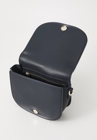 Námořnická kožená taška přes rameno s zaobleným klopou, zlatými detaily, vnitřní kapsou na zip a nastavitelým popruhem pro všestrannost.