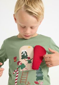 Grøn bomulds T-shirt med festlig illustration af en julescene, rød handskeaccent, med figurer og træer i forskellige farver.