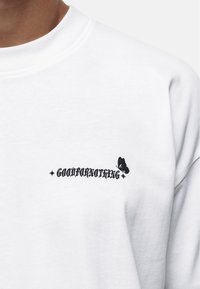 Biała bluza z czarnym napisem "GOODFORNOTHING" i graficznym motylem. Wykonana z miękkiego materiału, z okrągłym dekoltem i luźnym fasonem.