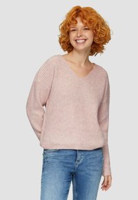 Maglione rosa a maglia con scollo a V, texture a coste e maniche lunghe, abbinato a jeans blu, che mostrano una vestibilità rilassata.