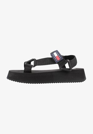 Mustat platform-sandaalit tekstuurilla varustetulla kumipohjalla, säädettävillä kangashihnoilla ja brändin logotunnuksella punaisilla, valkoisilla ja sinisillä yksityiskohdilla.