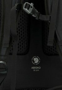 Il retro in rete nera di uno zaino presenta cinghie regolabili e una fibbia grigia. Include l'etichetta "ABISKO 35 S/M" e un logo del marchio.