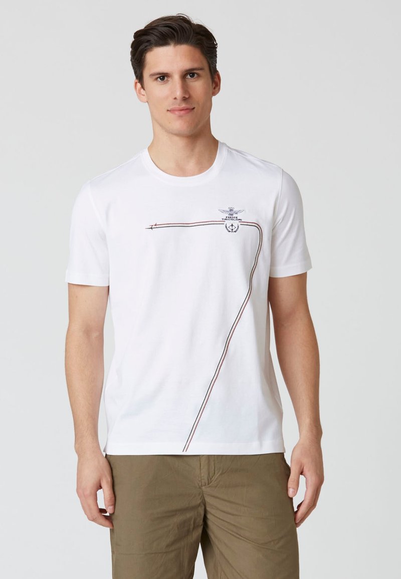 T-shirt bianco a maniche corte in cotone, con un design rosso e marrone e un'emblema sulla parte superiore sinistra. Classico scollo rotondo.