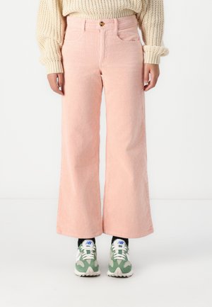 Pantaloni in corduroy rosa a gamba larga con righe verticali, chiusura a bottone, tasche frontali, abbinati a sneaker verdi e bianche.