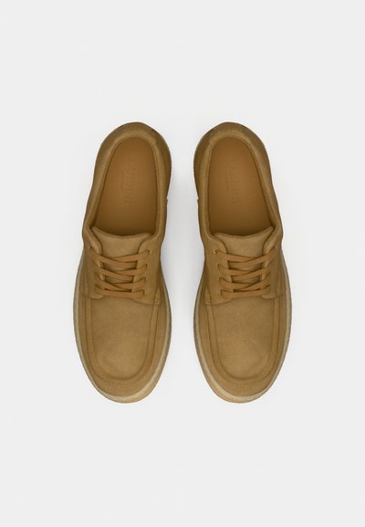 Pantofi bej din piele întoarsă, cu vârf rotund, design cu șireturi și branț amortizat. Prezintă un panou lateral texturat și o talpă în contrast.