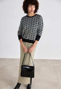 Svart og hvit DKNY-logo genser, strikket stoff, lange ermer. Olivengrønn skjørt, ankellangt. Svart veske med stropp, blank overflate.